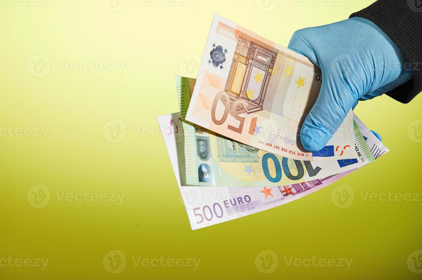 handen på en man i en blå medicinsk handske håller pengar i form av euroräkningar på gul bakgrund foto