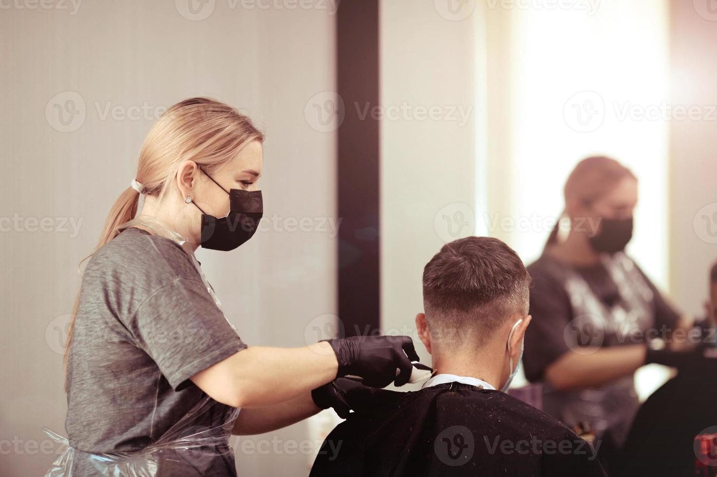 frisör med säkerhet åtgärder för covid19, nedskärningar en man i en medicin mask, social distans, skärande hår med en medicinsk mask och sudd handskar. foto