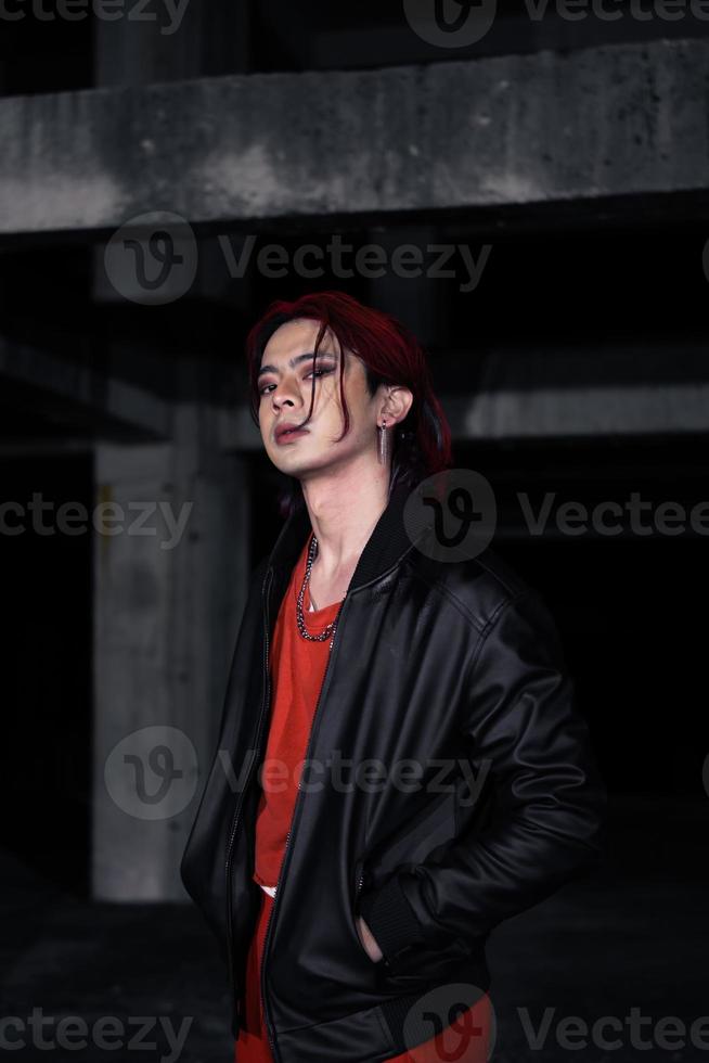 ett asiatisk man med röd hår och en svart jacka är Framställ i ett övergiven byggnad foto