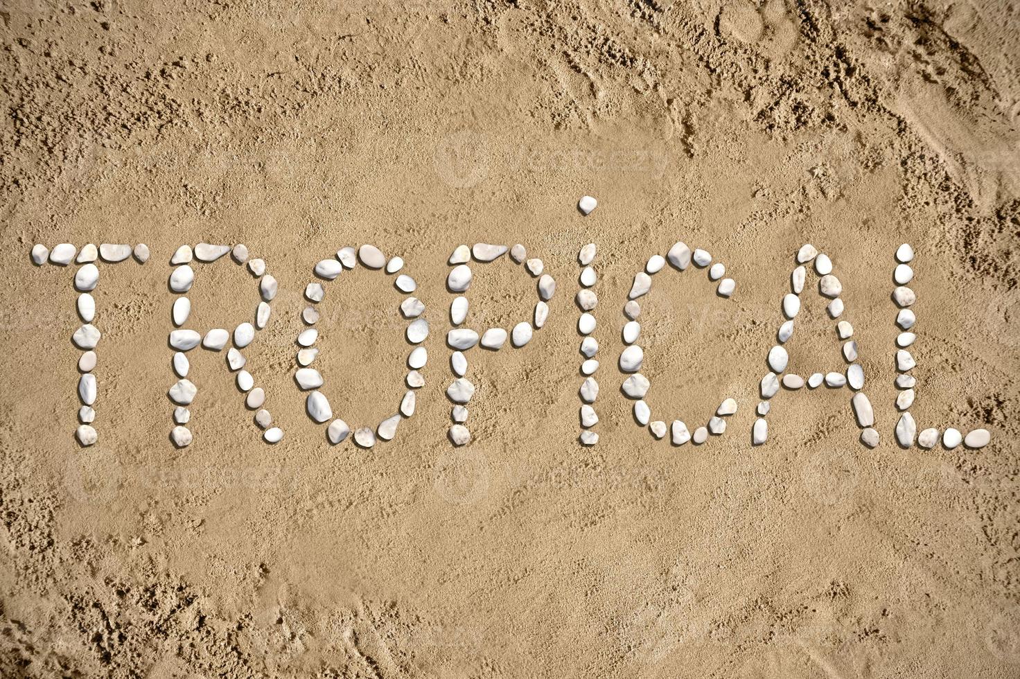 tropisk - ord tillverkad med stenar på sand foto