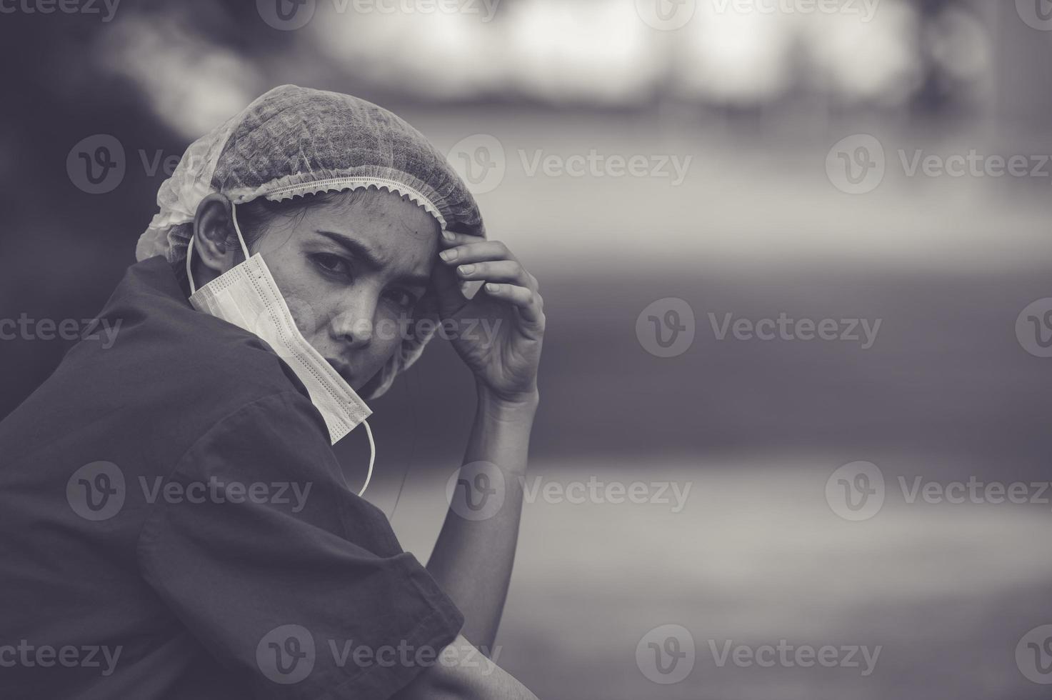 trött deprimerad kvinnlig asiatisk skrubbsköterska bär ansiktsmask blå uniform sitter på sjukhusgolvet, ung kvinna läkare stressad av hårt arbete foto