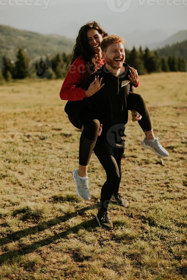 ung kvinna ridning piggyback på en pojkvän på grön kullar foto