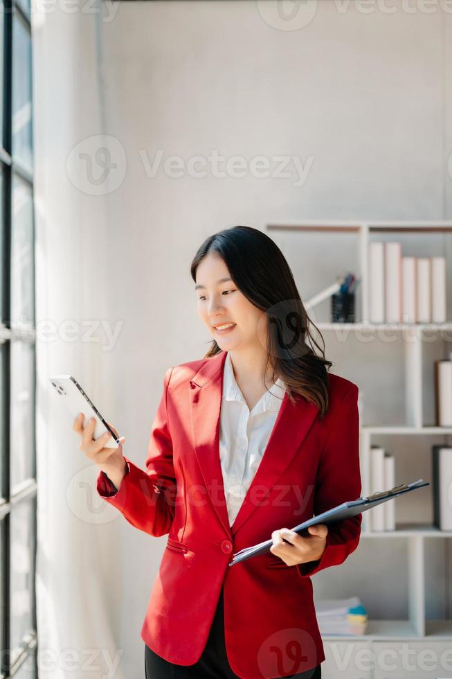 självsäker företag expert- attraktiv leende ung kvinna skriver bärbar dator ang innehav digital läsplatta på skrivbord i kreativ kontor. foto