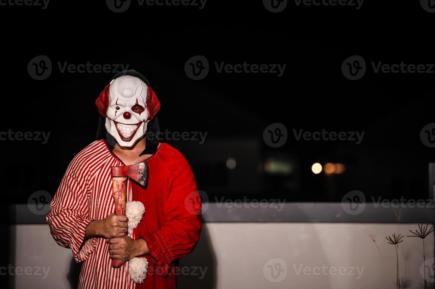 asiatisk stilig man ha på sig clown mask med vapen på de natt scen, halloween festival koncept, skräck skrämmande Foto av en mördare i orange tyg, ondska clown charactor