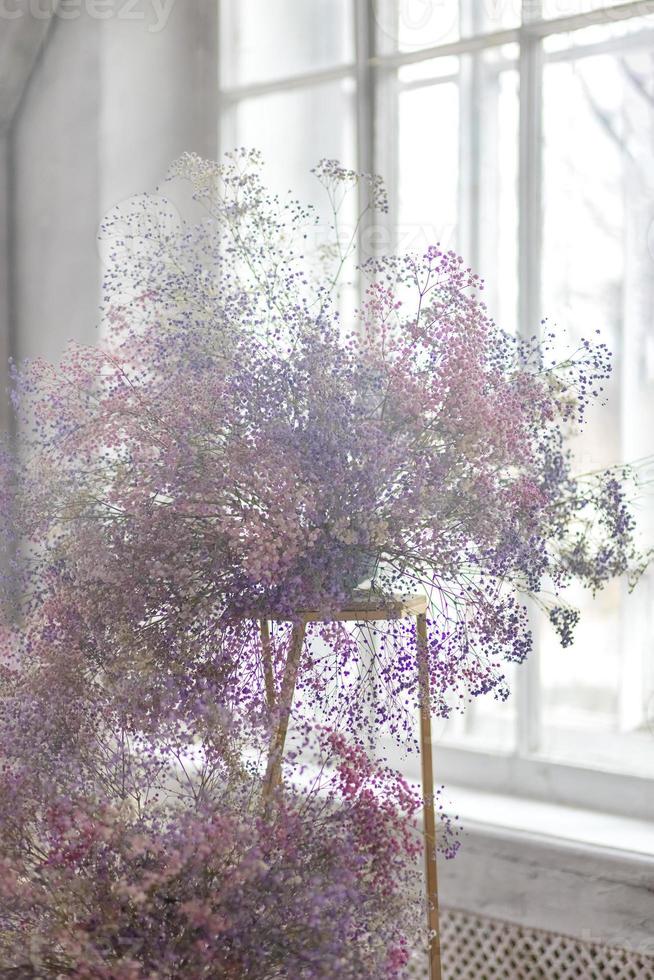 en säng i en ljus sovrum i pastell färger i boho stil, de trender Färg av 2023. de rum är dekorerad med lila och rosa Gypsophila blommor, årgång dekor i de rum i retro loft stil. foto