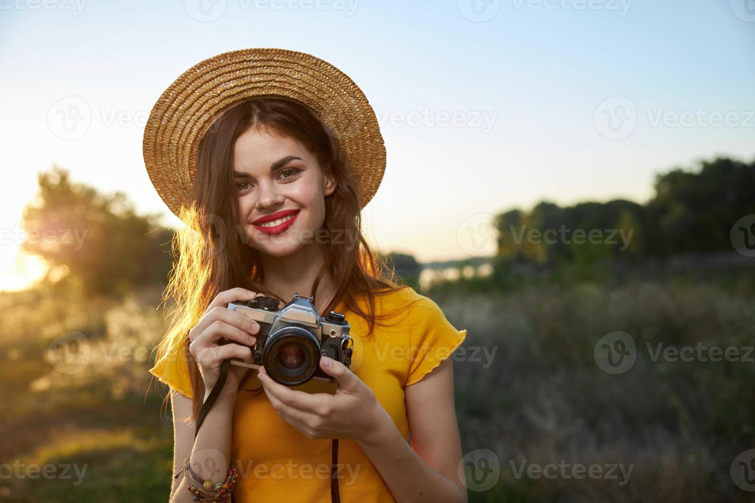 kvinna fotograf kamera i händer leende röd mun hatt attraktiv se natur foto