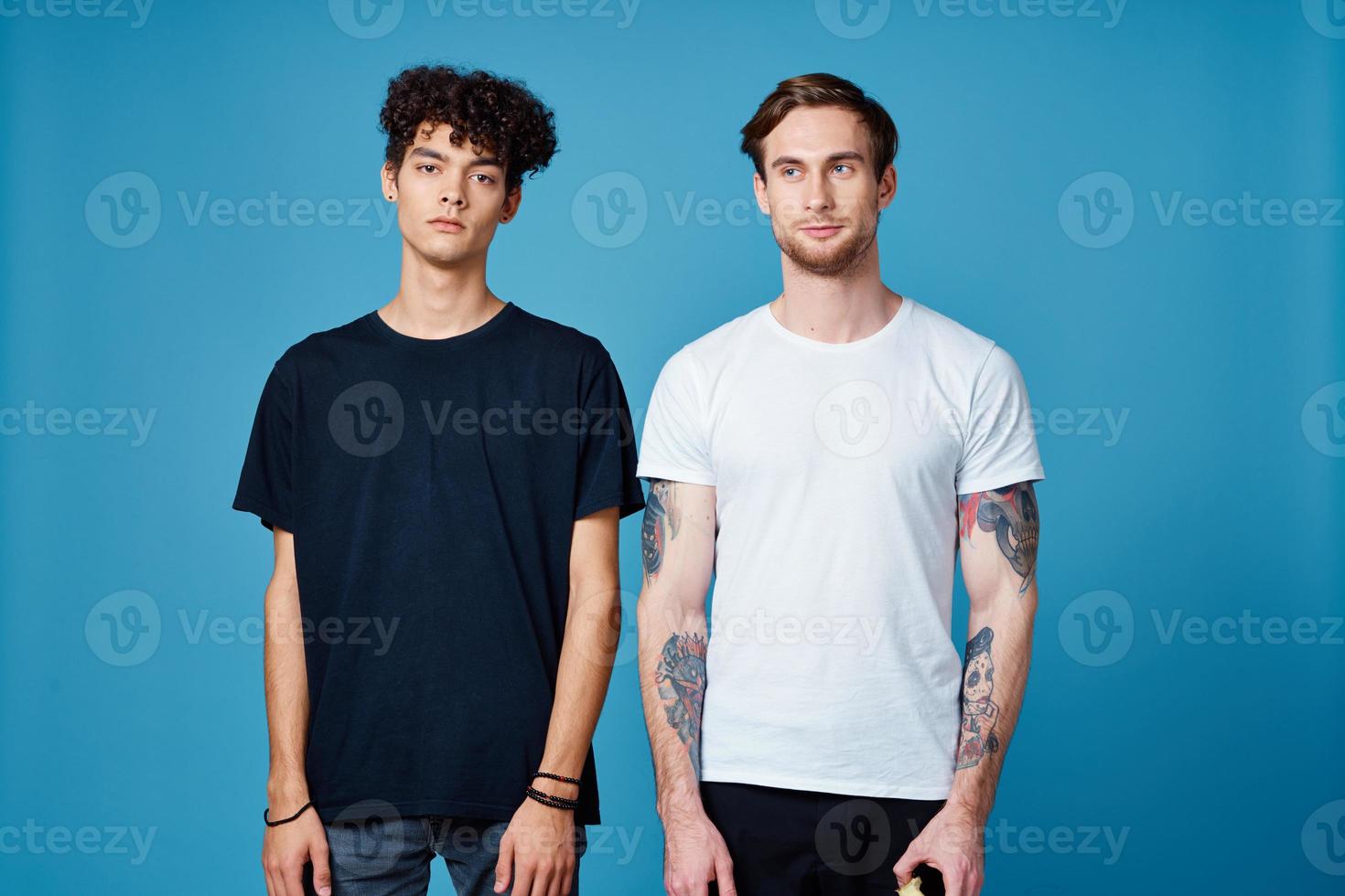 lockigt kille i en svart t-shirt och en man med en tatuering på en blå bakgrund vänner chattar foto