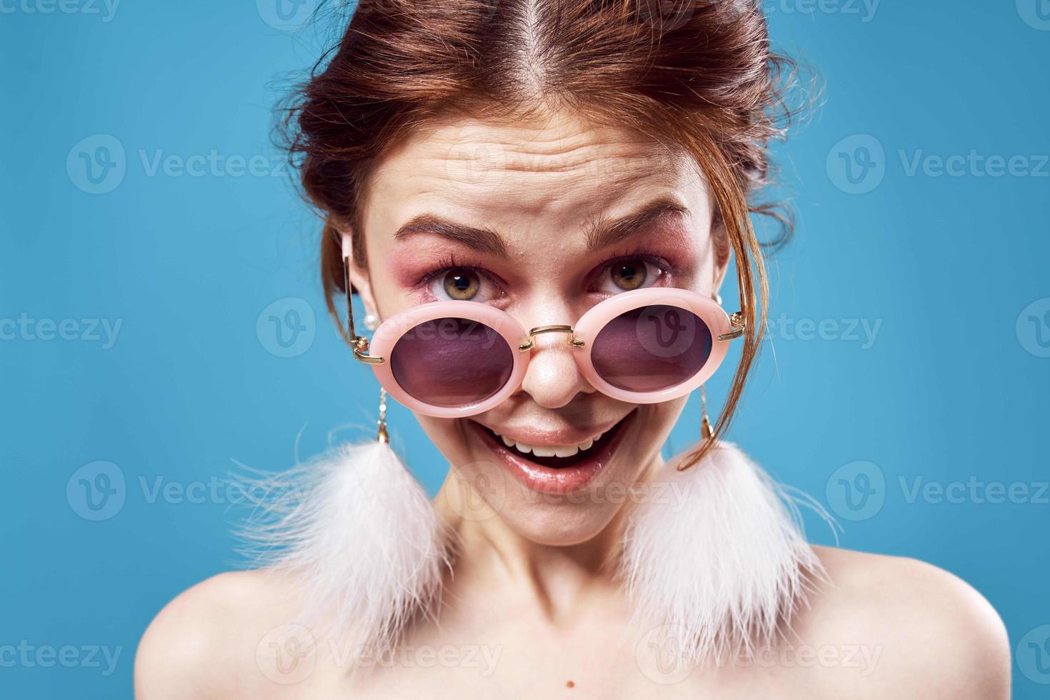 emotionell kvinna bär solglasögon fluffig örhängen Smycken närbild blå bakgrund foto