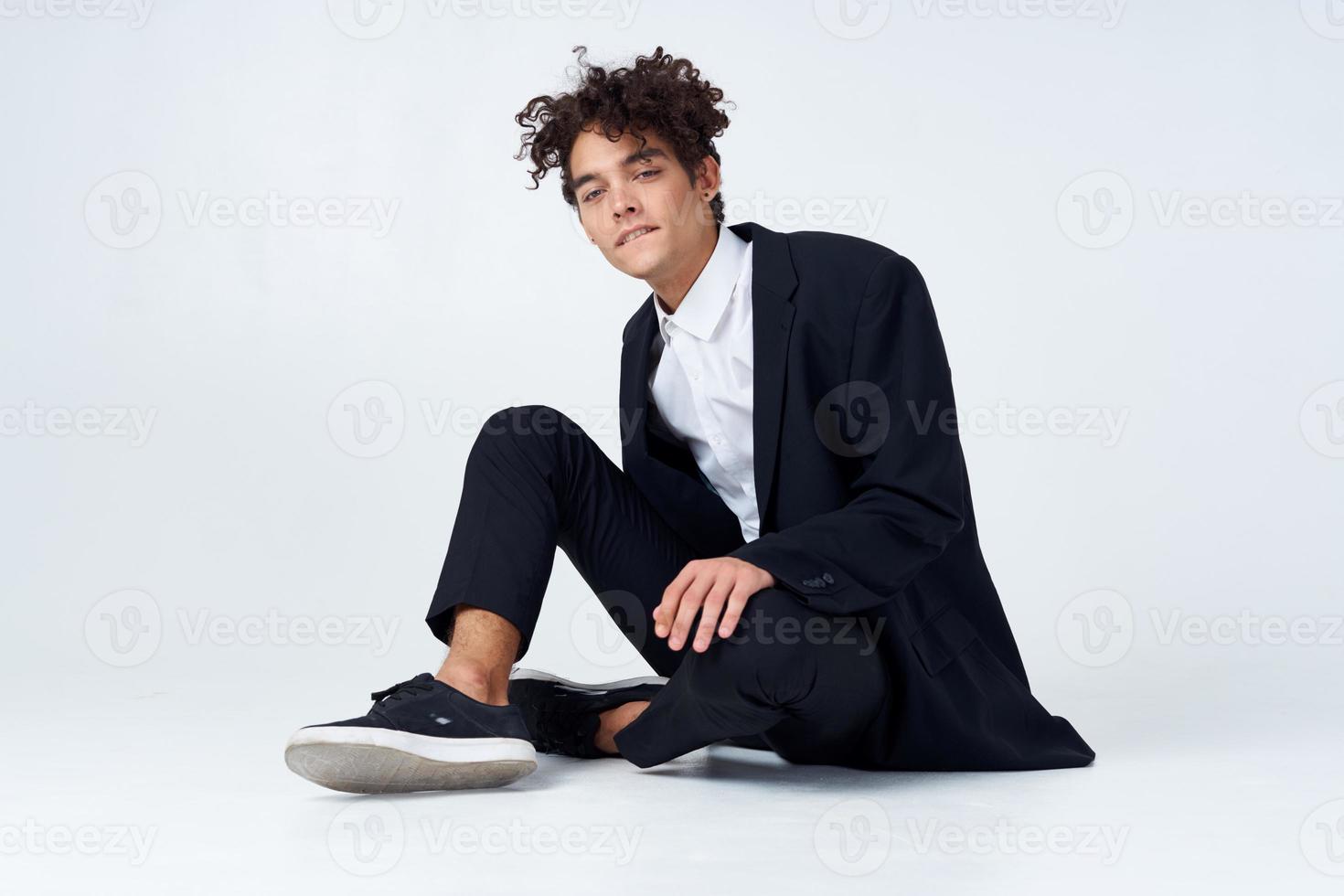 eleganta ung man i kostym sitter på de golv och gymnastikskor lockigt hår mode foto