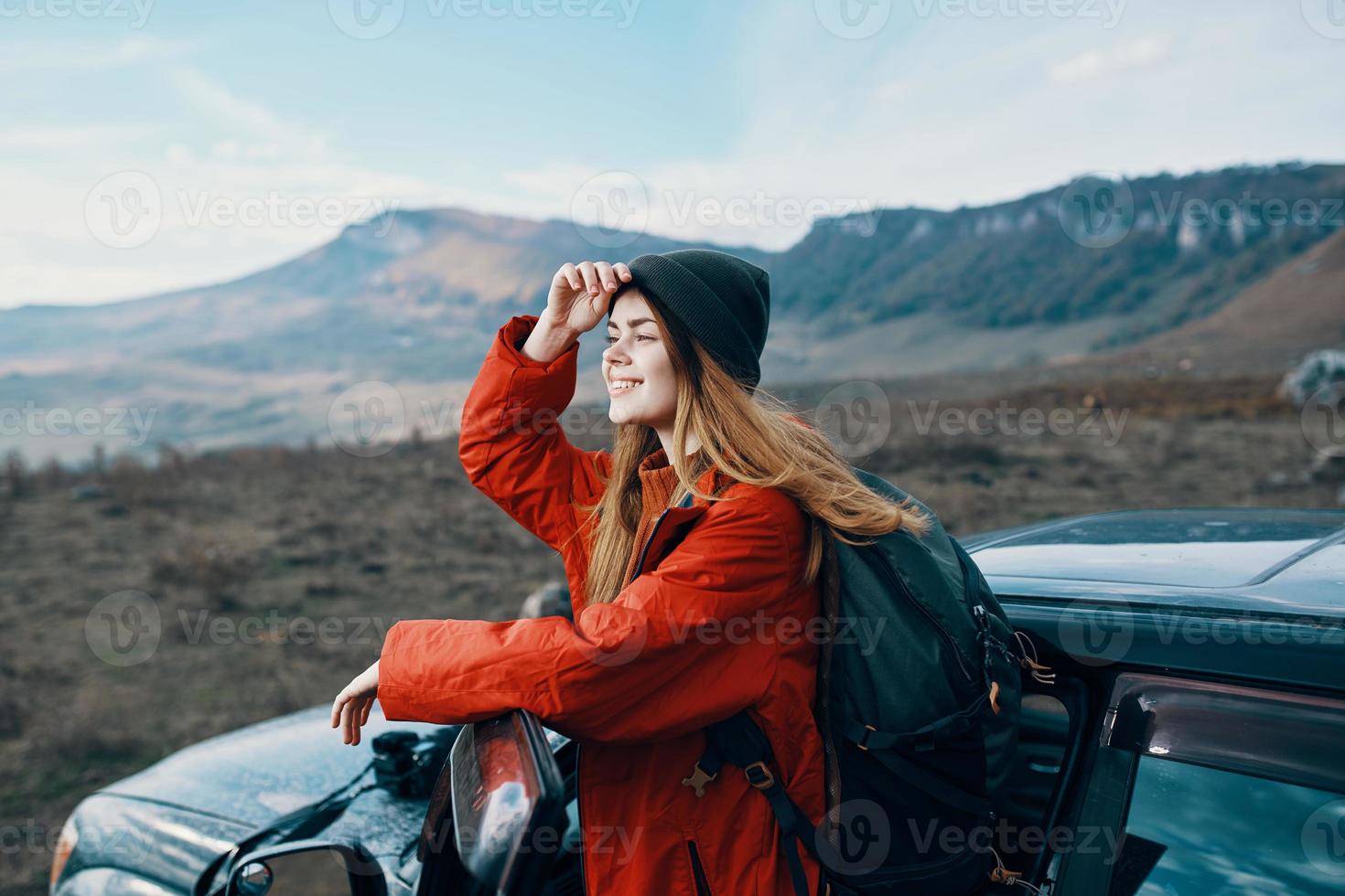 kvinna i en hatt med en ryggsäck på henne tillbaka lutade på de dörr av en bil i de bergen utomhus foto