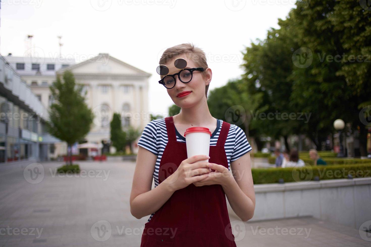 kvinna med kort hår och en glas av kaffe gående utomhus färsk luft foto