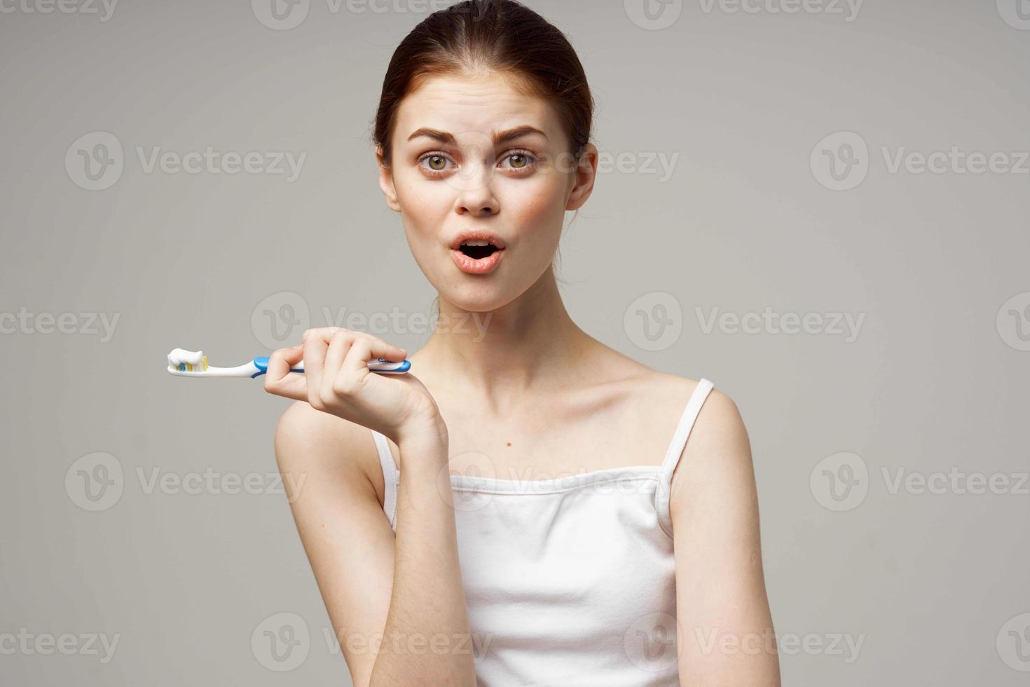glad kvinna med en tandborste i hand morgon- hygien ljus bakgrund foto