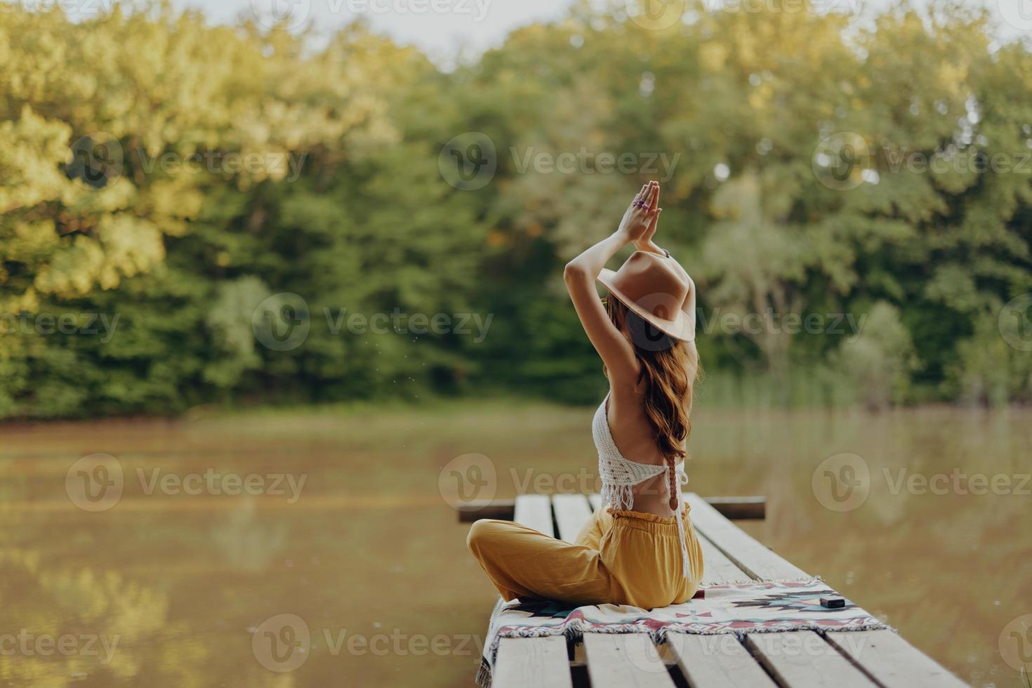 en kvinna yogi sitter med henne tillbaka till de flodbank på en bro och mediterar på avkopplande henne kropp i natur foto