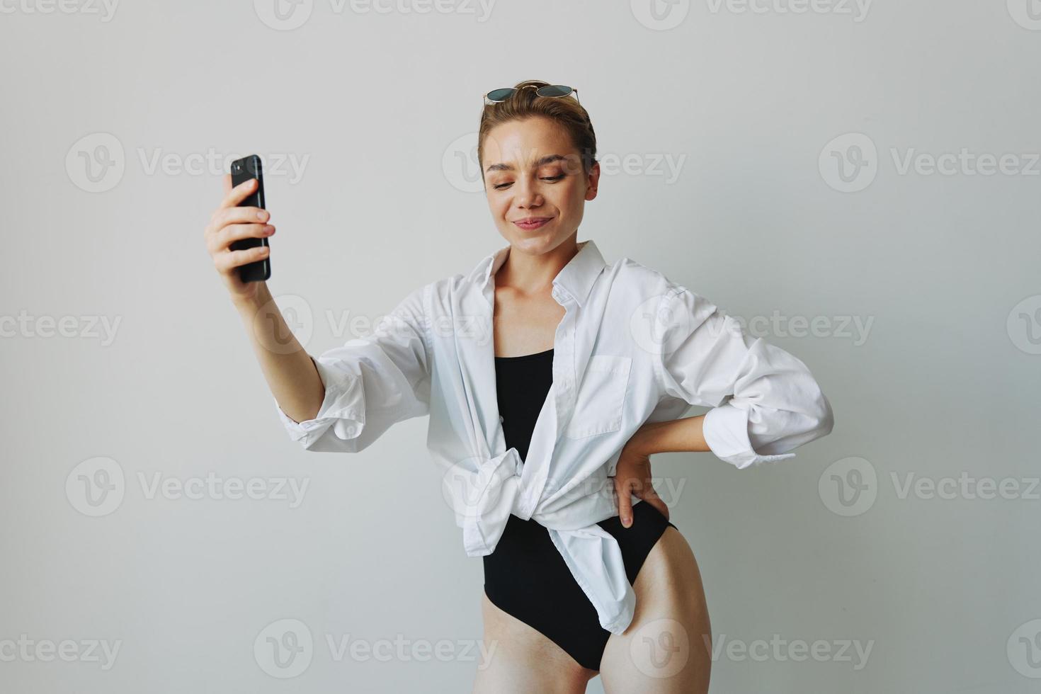 Tonårs flicka bloggare tar foton och skott. själv på video på henne telefon för social media innehåll, video bloggare, selfies mot en vit vägg med en leende på Hem, frilansare