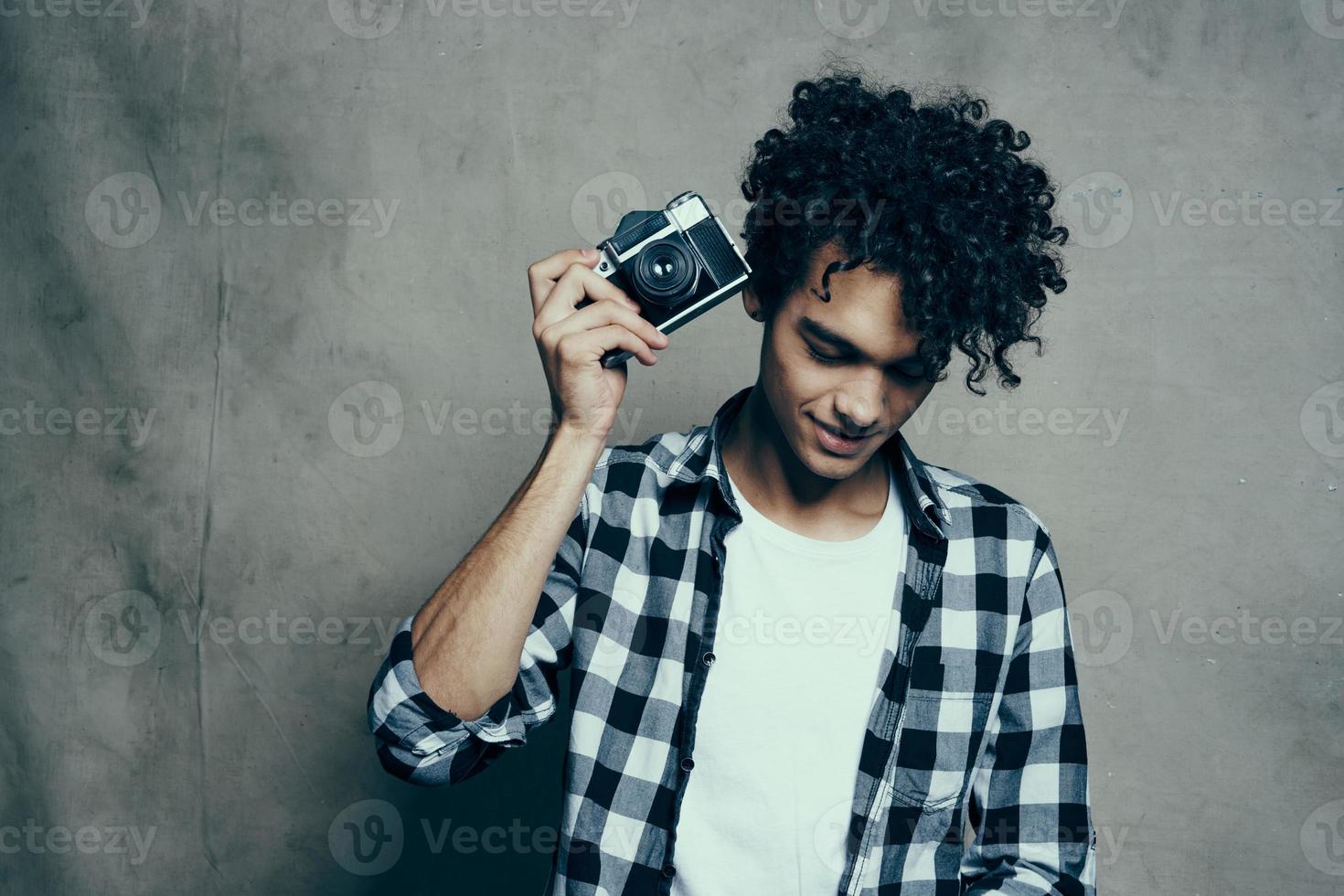 ung man med en kamera i hand och i en pläd t-shirt på en grå bakgrund inomhus fotograf foto