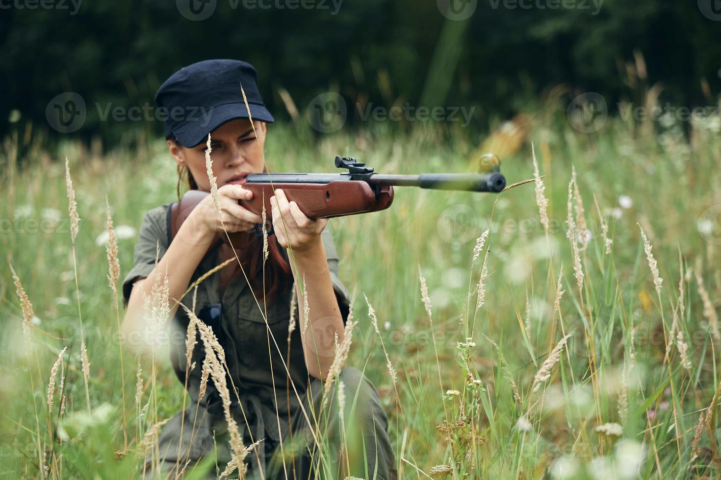 kvinna soldat med en vapen i omslag, en svart keps jakt vapen grön foto