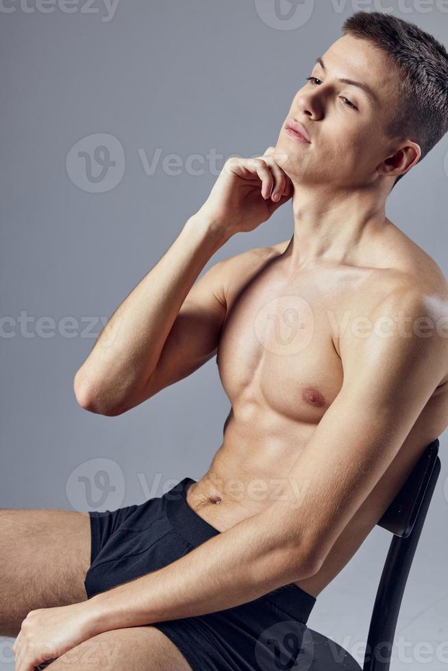 trevlig kille med en pumpade upp naken torso i svart trosor sitter på en stol foto