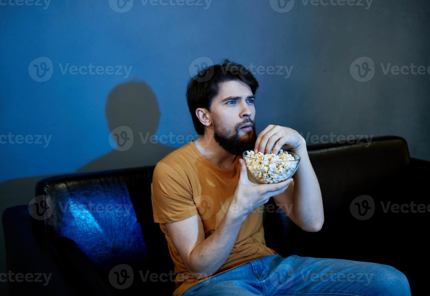 ensam man Sammanträde på soffa med popcorn plattor grå vägg foto