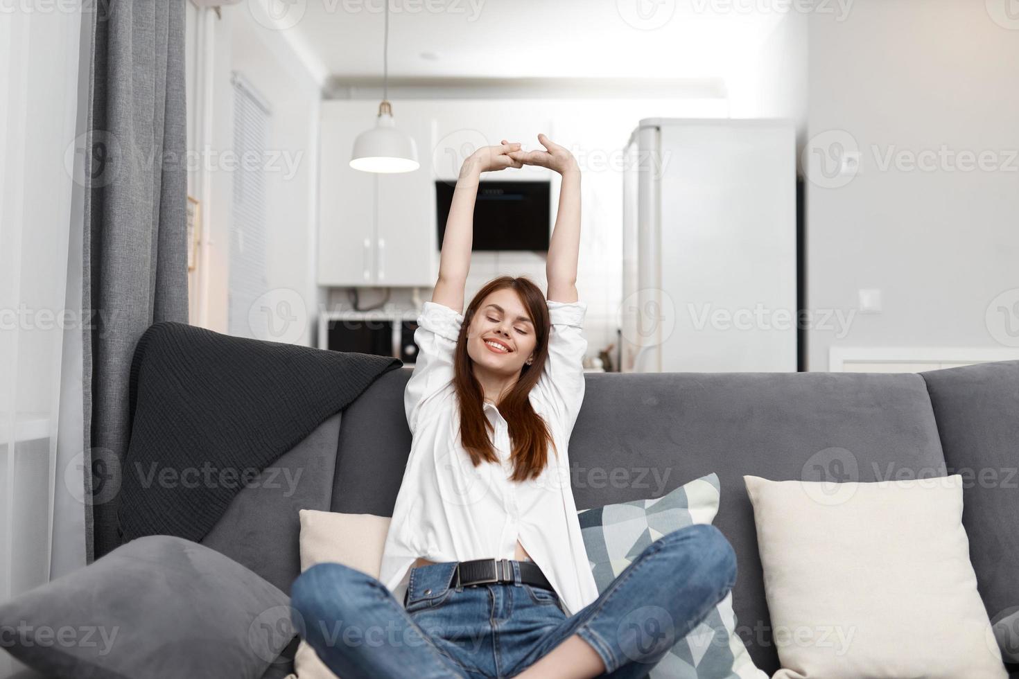 glad kvinna stretching själv medan Sammanträde på de soffa vilar lägenhet interiör foto