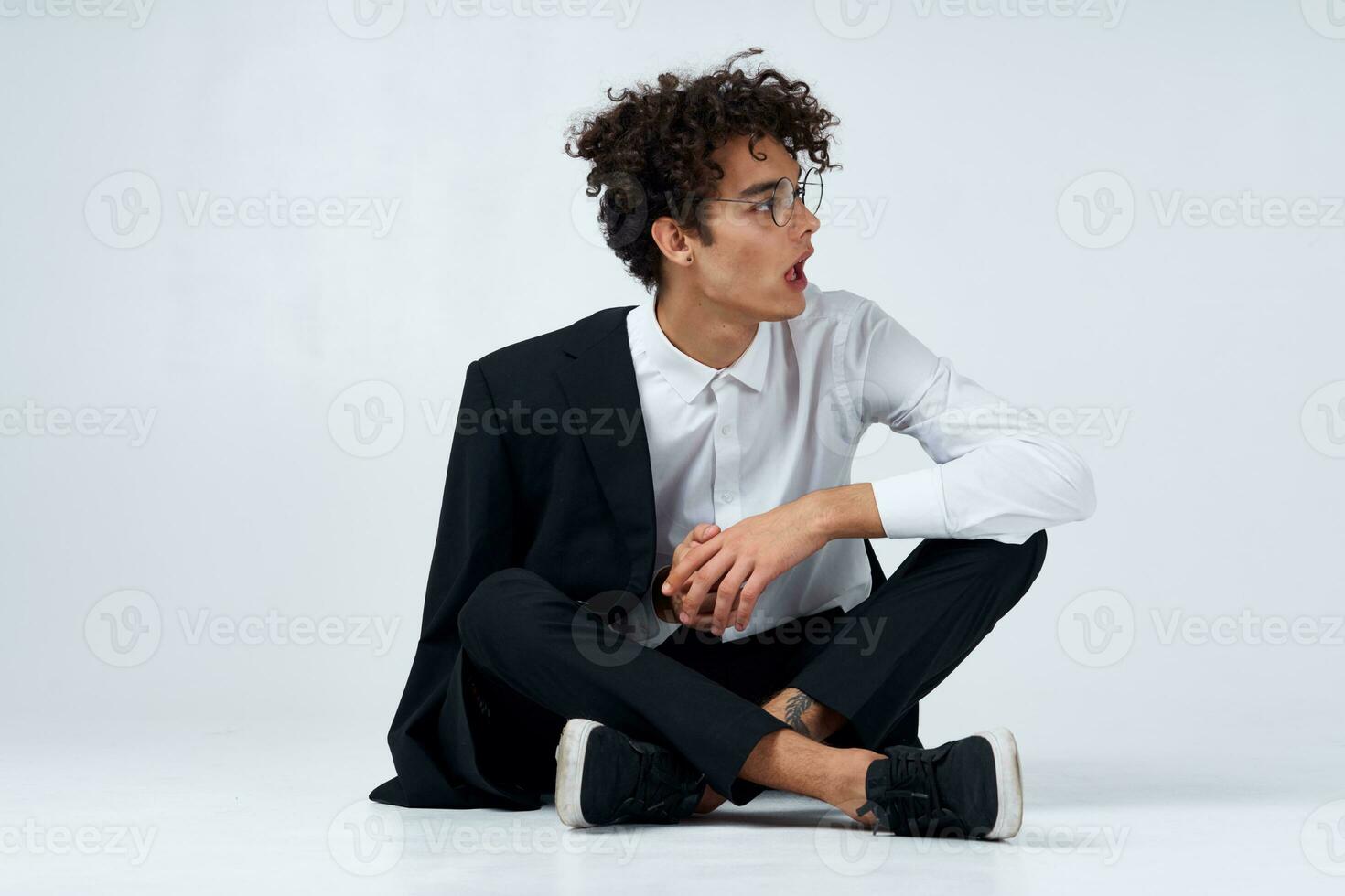 emotionell kille i en klassisk kostym sitter på de golv i en ljus rum glasögon på de ansikte porträtt modell foto