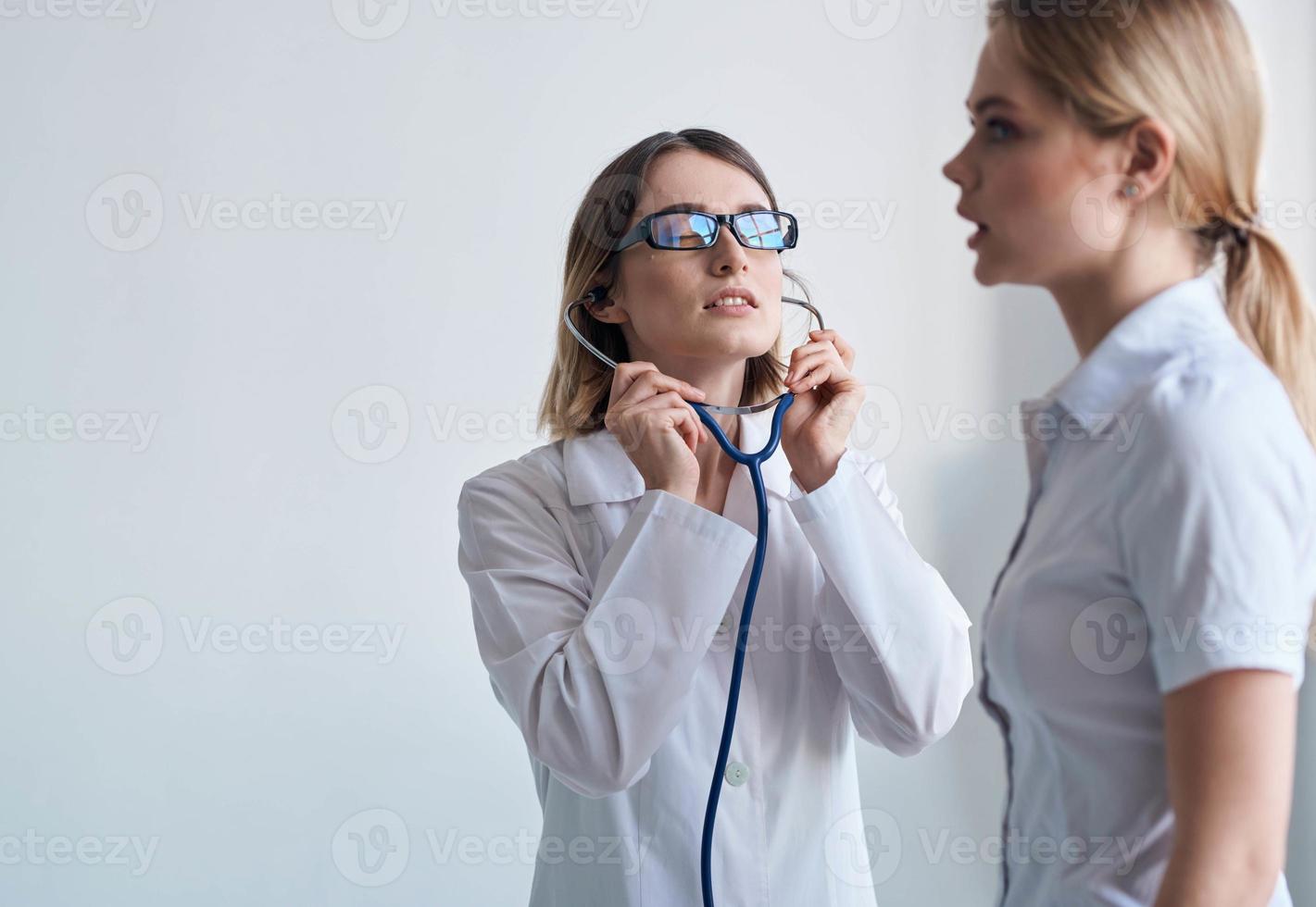 kvinna läkare i en medicinsk klänning och glasögon med en stetoskop runt om henne nacke och en kvinna patient foto