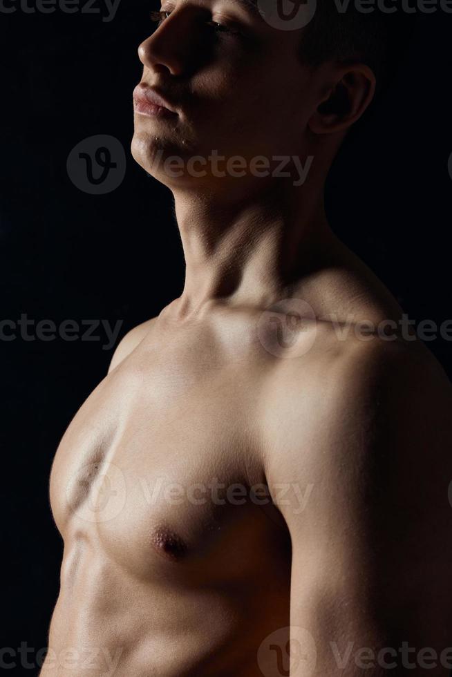 sexig kroppsbyggare med naken torso på svart bakgrund porträtt sida se foto
