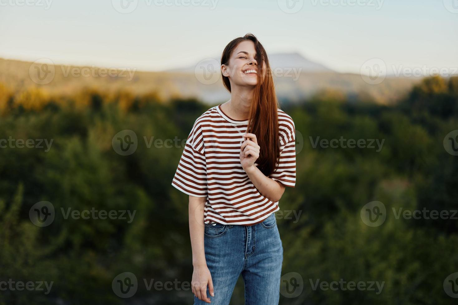 en ung kvinna skrattar och utseende på de kamera i enkel kläder mot de bakgrund av en skön landskap av bergen och träd i höst foto