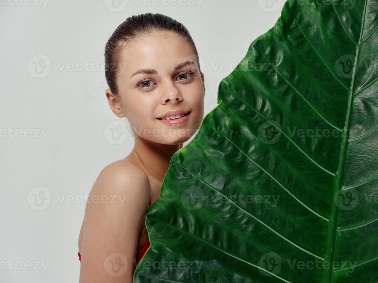 kvinna innehav grön blad av handflatan träd på ljus bakgrund beskurna se av röd t-shirt foto