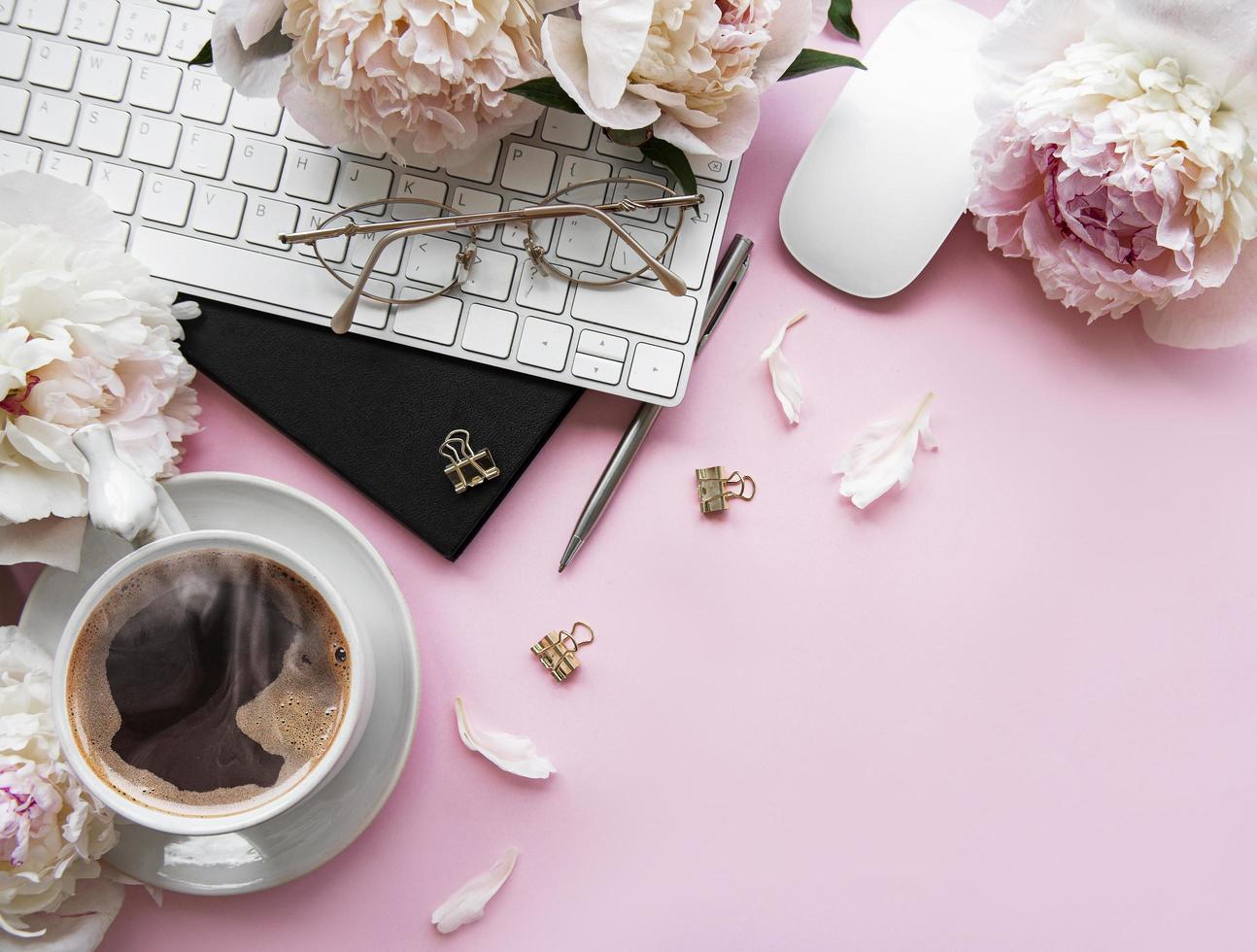 platt låg ovanifrån kvinnors kontorsskrivbord med blommor och tillbehör på rosa bakgrund foto