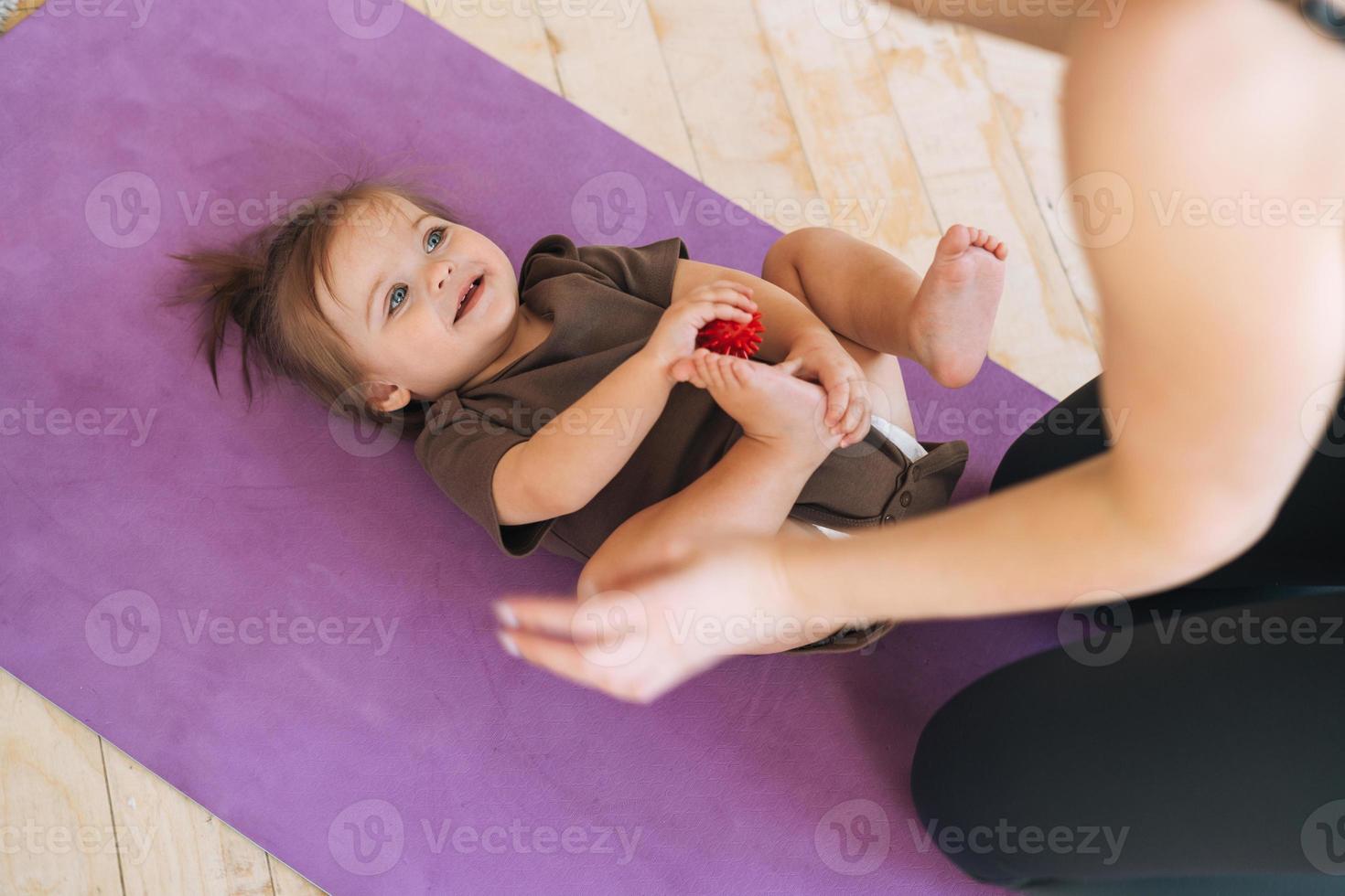 ung kvinna passa mamma med bebis flicka håller på med övningar med massage boll på matta på Hem foto