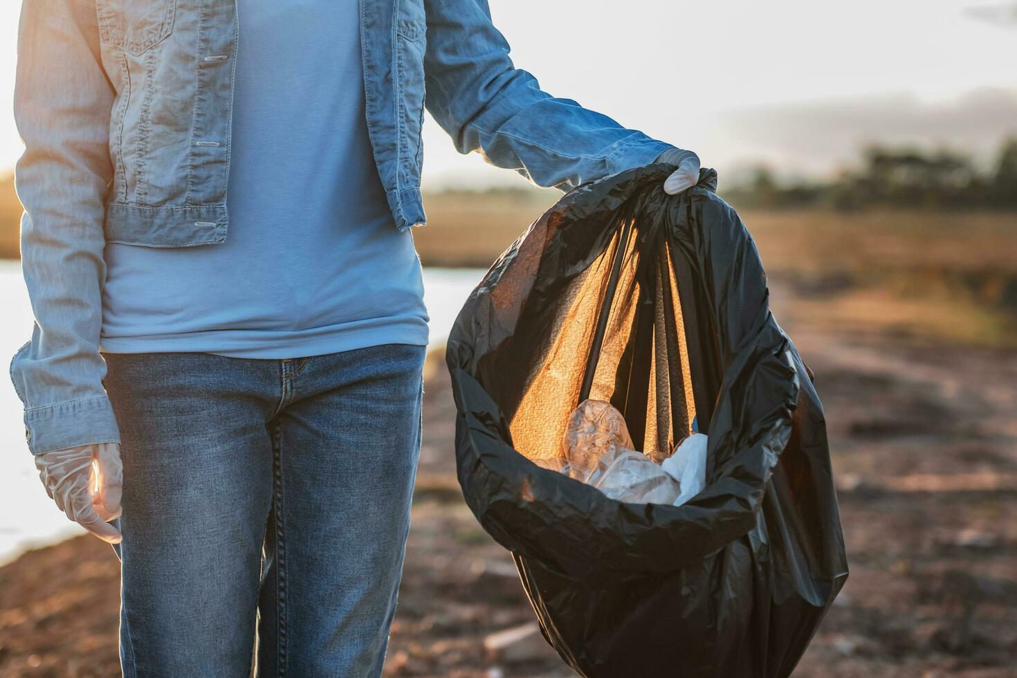 människor volontär- förvaring sopor plast och glas flaska in i svart väska på parkera flod i solnedgång foto