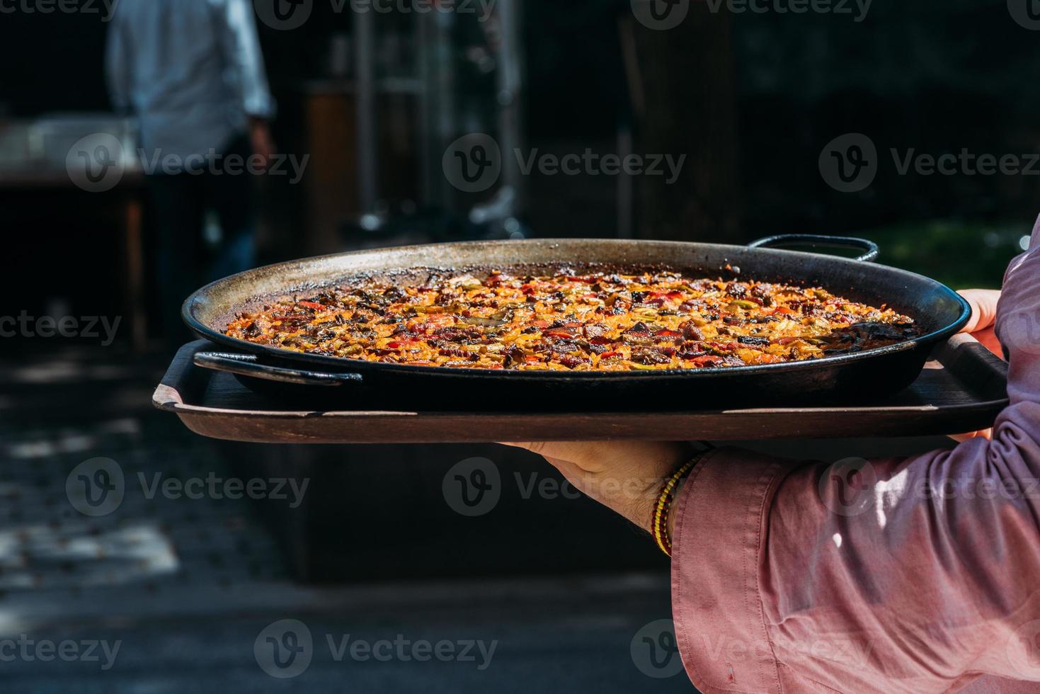 servitör innehav en jätte spanska paella maträtt utanför en restaurang terrass foto