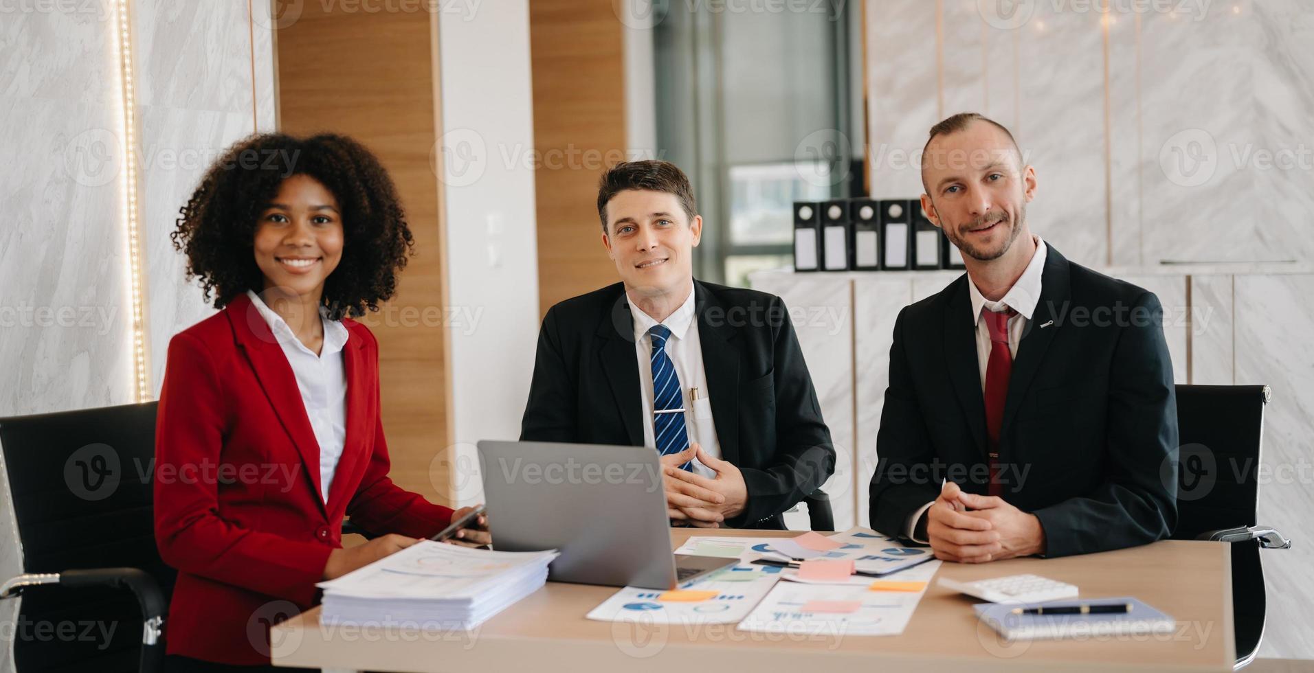 Lycklig affärsmän medan samarbetande på en ny projekt i ett kontor. grupp av olika affärsmän använder sig av en bärbar dator och läsplatta i kontor. foto