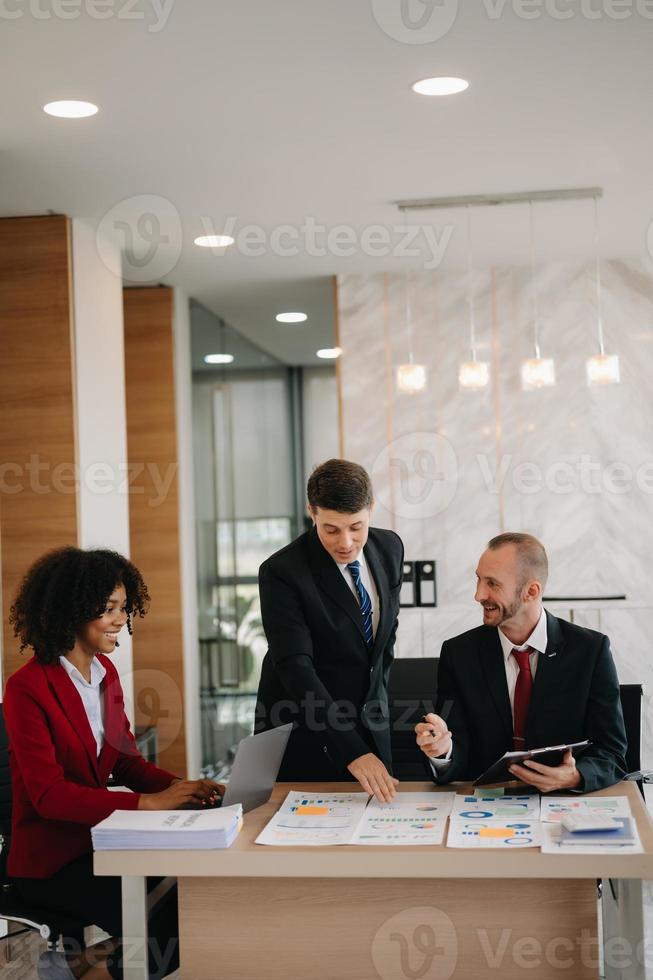 Lycklig affärsmän medan samarbetande på en ny projekt i ett kontor. grupp av olika affärsmän använder sig av en bärbar dator och läsplatta i kontor. foto