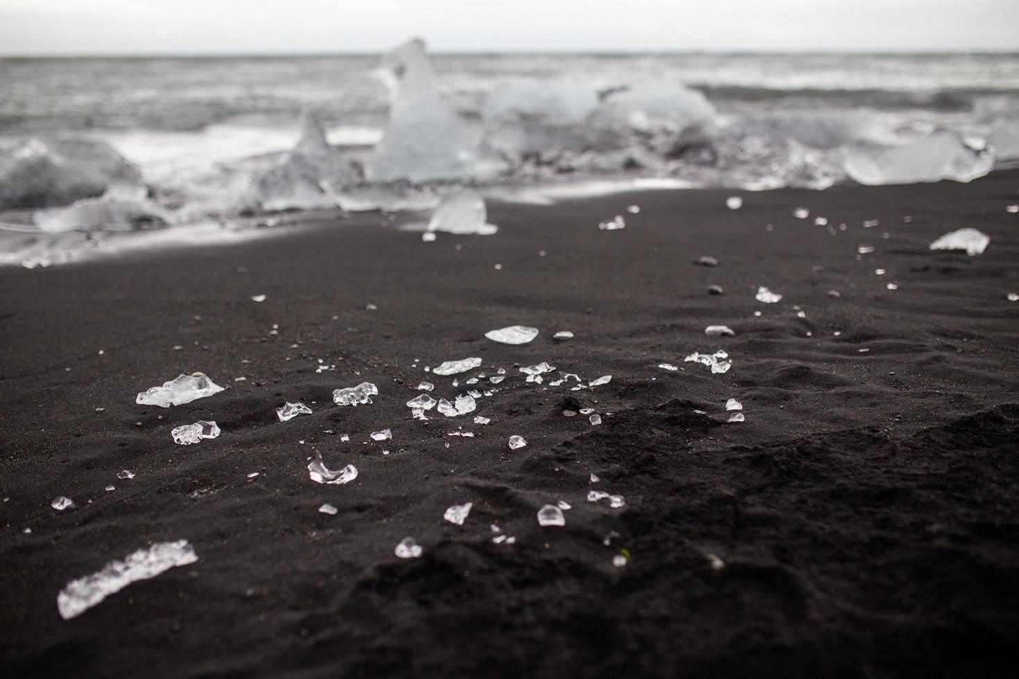 små isbitar på svart sandstrand i vik, island foto