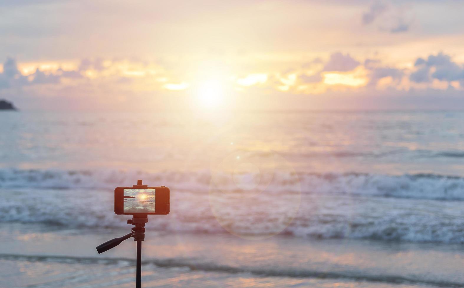 någon som reser på patong beach, phuket, thailand med en mobiltelefon på ett stativ som väntar på att solnedgången ska ta ett bra foto