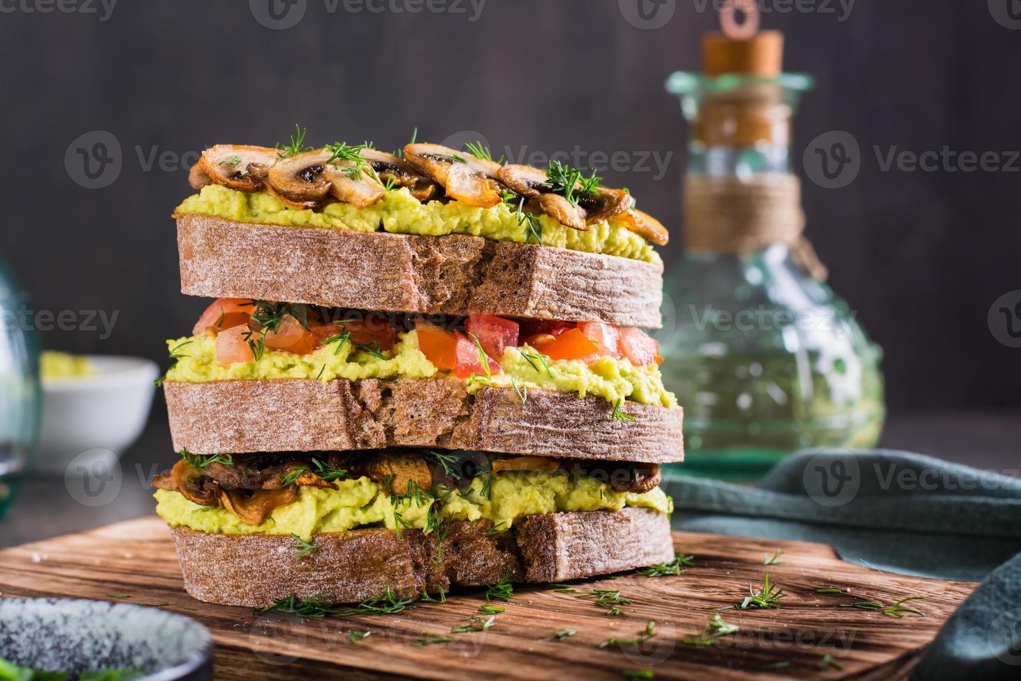 närbild av en skiktad råg bröd smörgås med guacamole, friterad svamp, tomater och dill foto