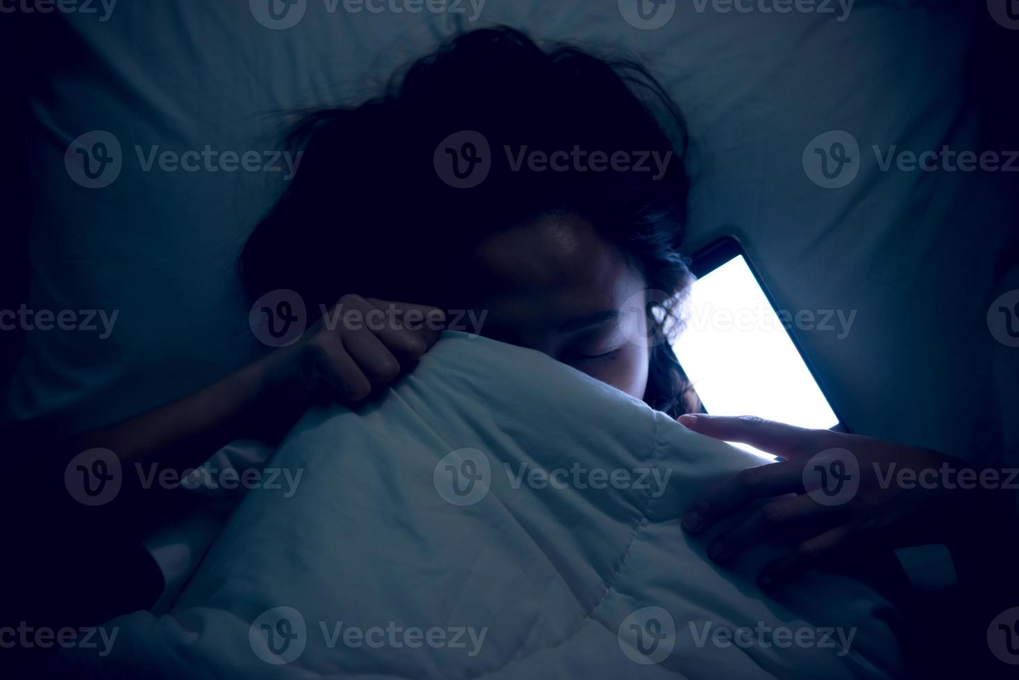 asiatisk unge spelar spel på smartphone i de säng på natten, den flicka missbrukare social media foto