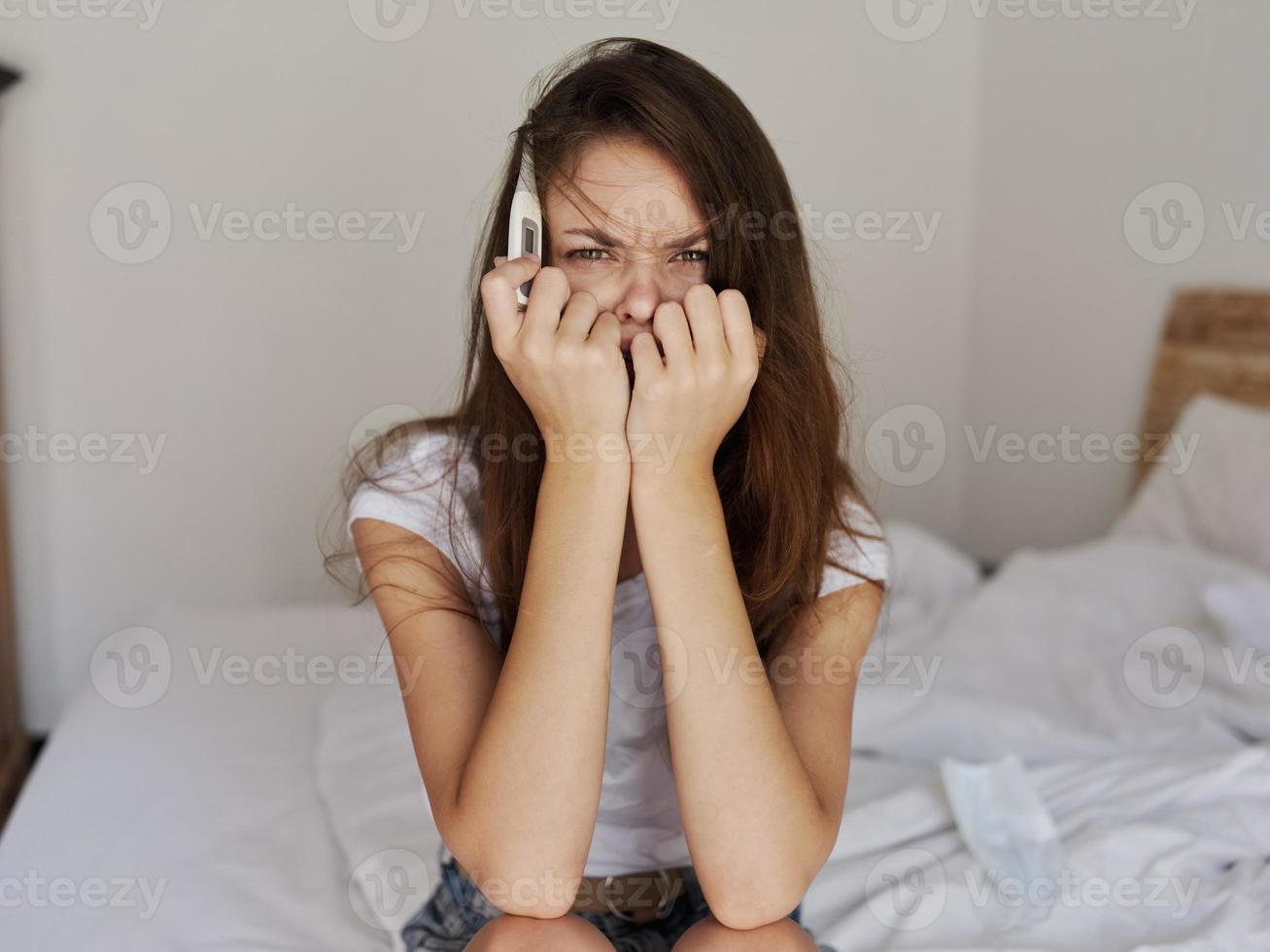 kvinna med en termometer i henne händer Sammanträde på de säng känsla oordning foto