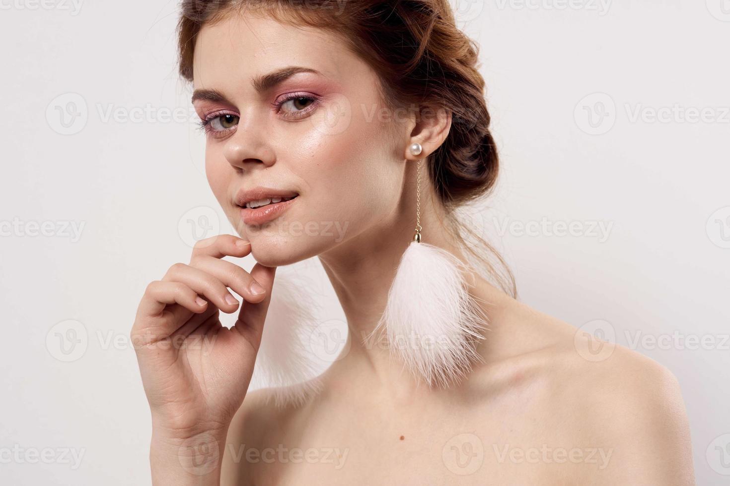 kvinna med bar axlar ljus smink fluffig örhängen mode ljus bakgrund foto