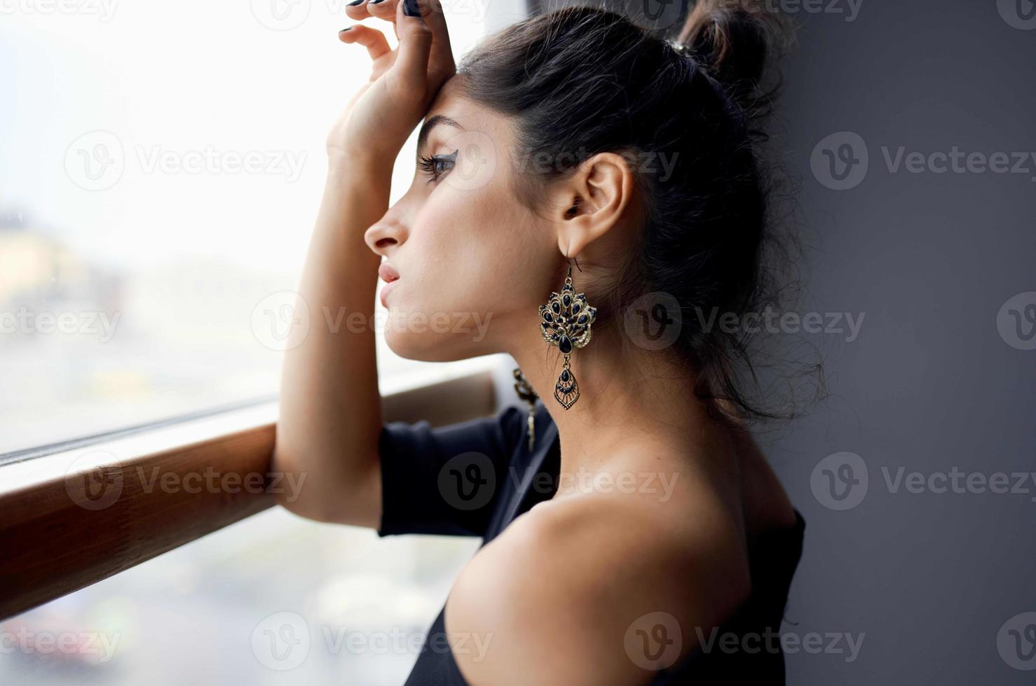 Söt kvinna nära fönster Framställ attraktiv se örhängen mode modell foto