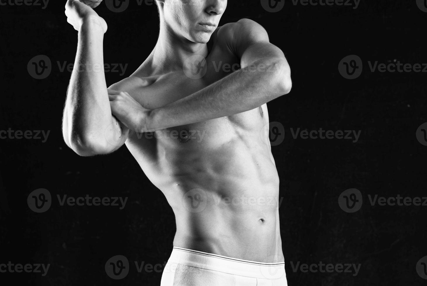kroppsbyggare med en pumpade upp kropp i vit trosor Framställ mörk bakgrund foto