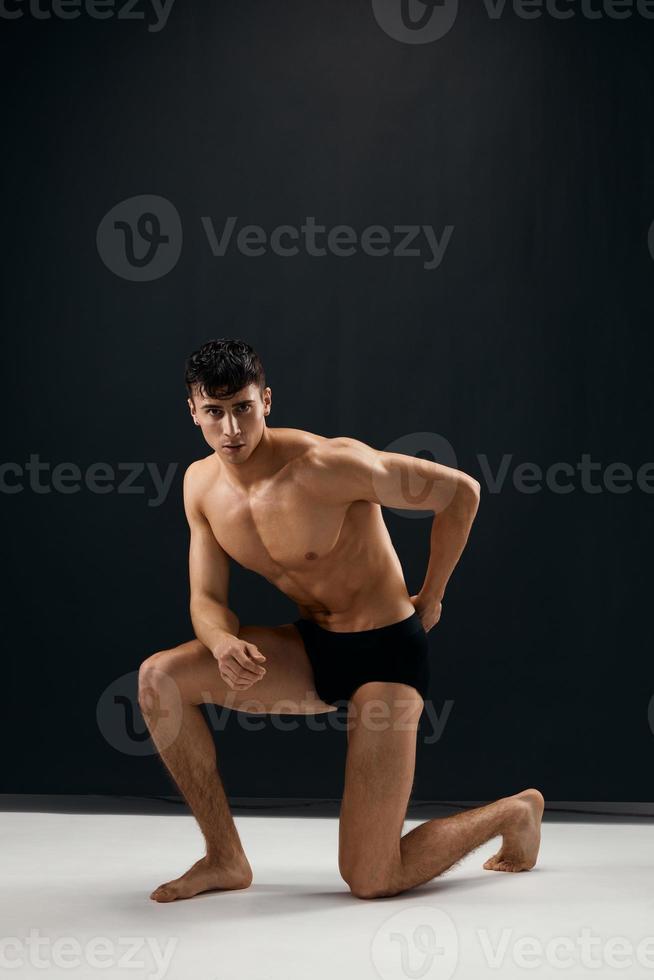 sportig man med pumpade upp muskulös kropp knäböjer Framställ mörk bakgrund foto