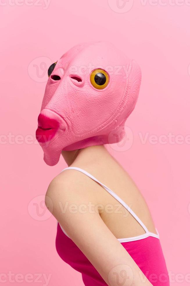 mager kvinna i en rosa halloween kostym med en fisk huvud på henne ansikte poser rolig mot en rosa bakgrund och utseende på de kamera, konst begrepp Foto