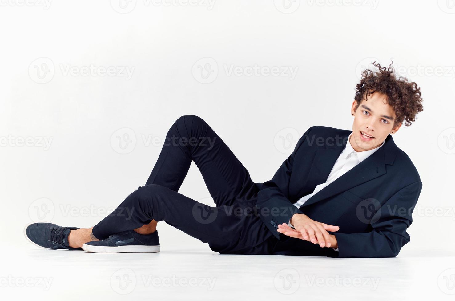 modern kille i en kostym och gymnastikskor Sammanträde på de golv i en ljus rum lockigt hår modell foto