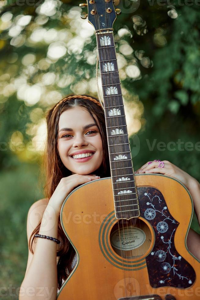 ung hippie kvinna med eco bild leende och ser in i de kamera med gitarr i hand i natur på en resa foto