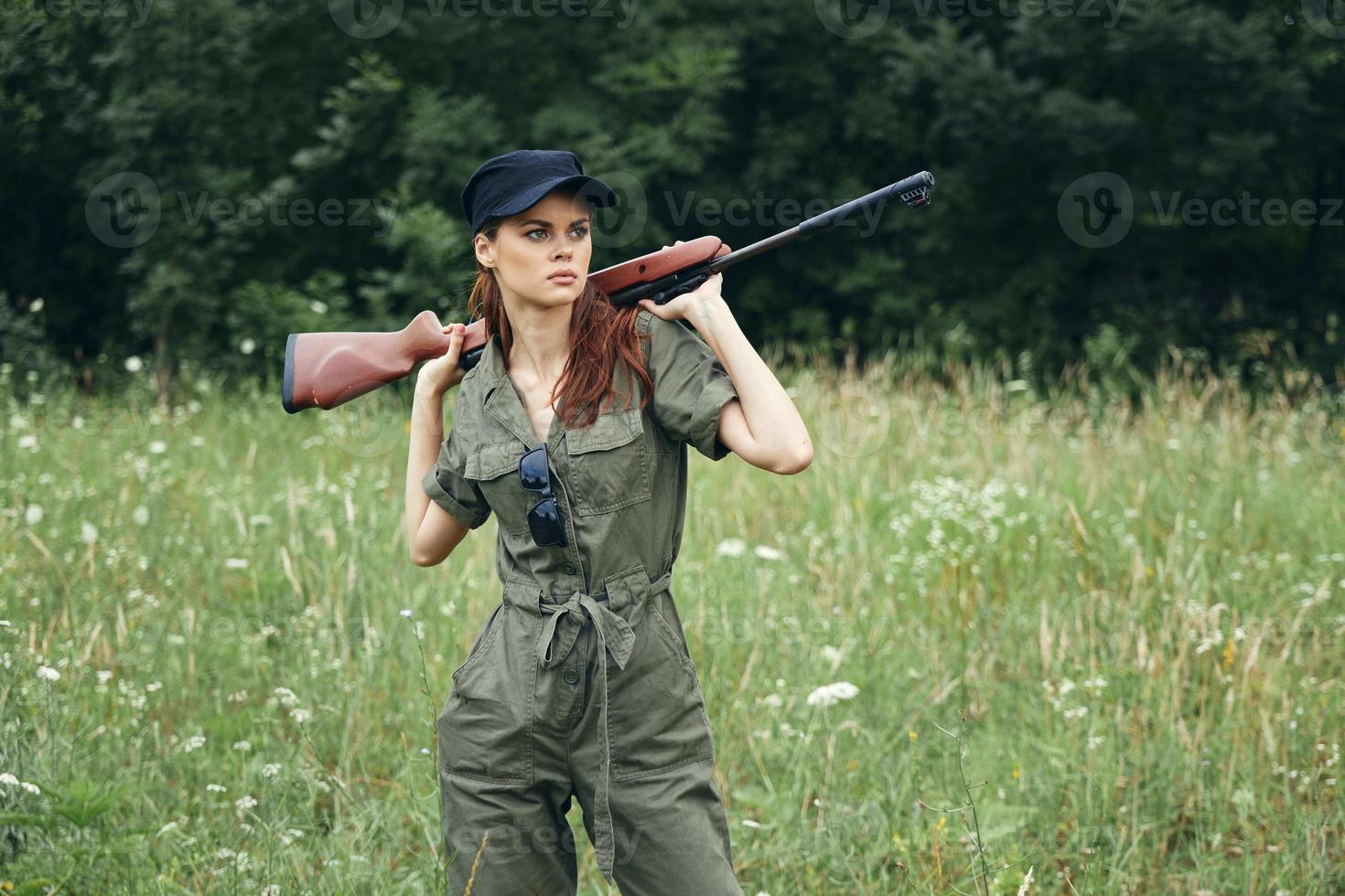 kvinna på utomhus- innehav en vapen i hans händer se åt sidan jakt grön löv foto