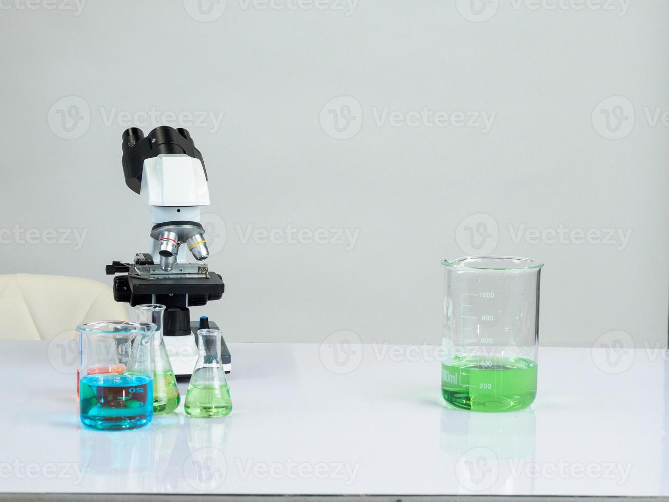 bägare och mikroskop för vetenskapsmän var placerad på en vit trä- tabell med forskning reagens i de ljus vit rum för studie och arbete foto