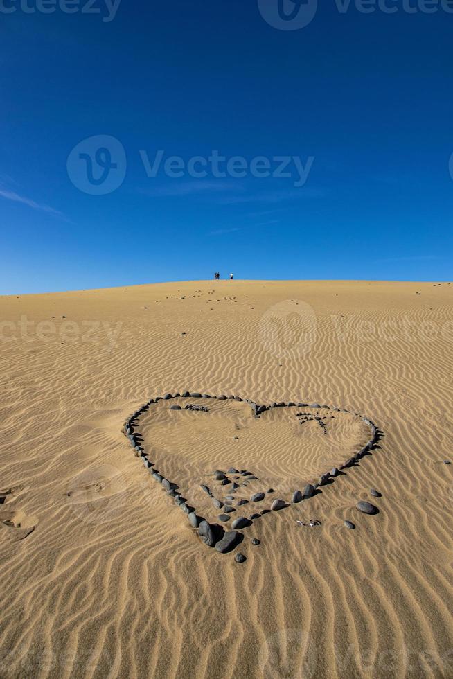 hjärta symbol av kärlek anordnad från grå sten på gyllene sand på en gyllene dyn foto