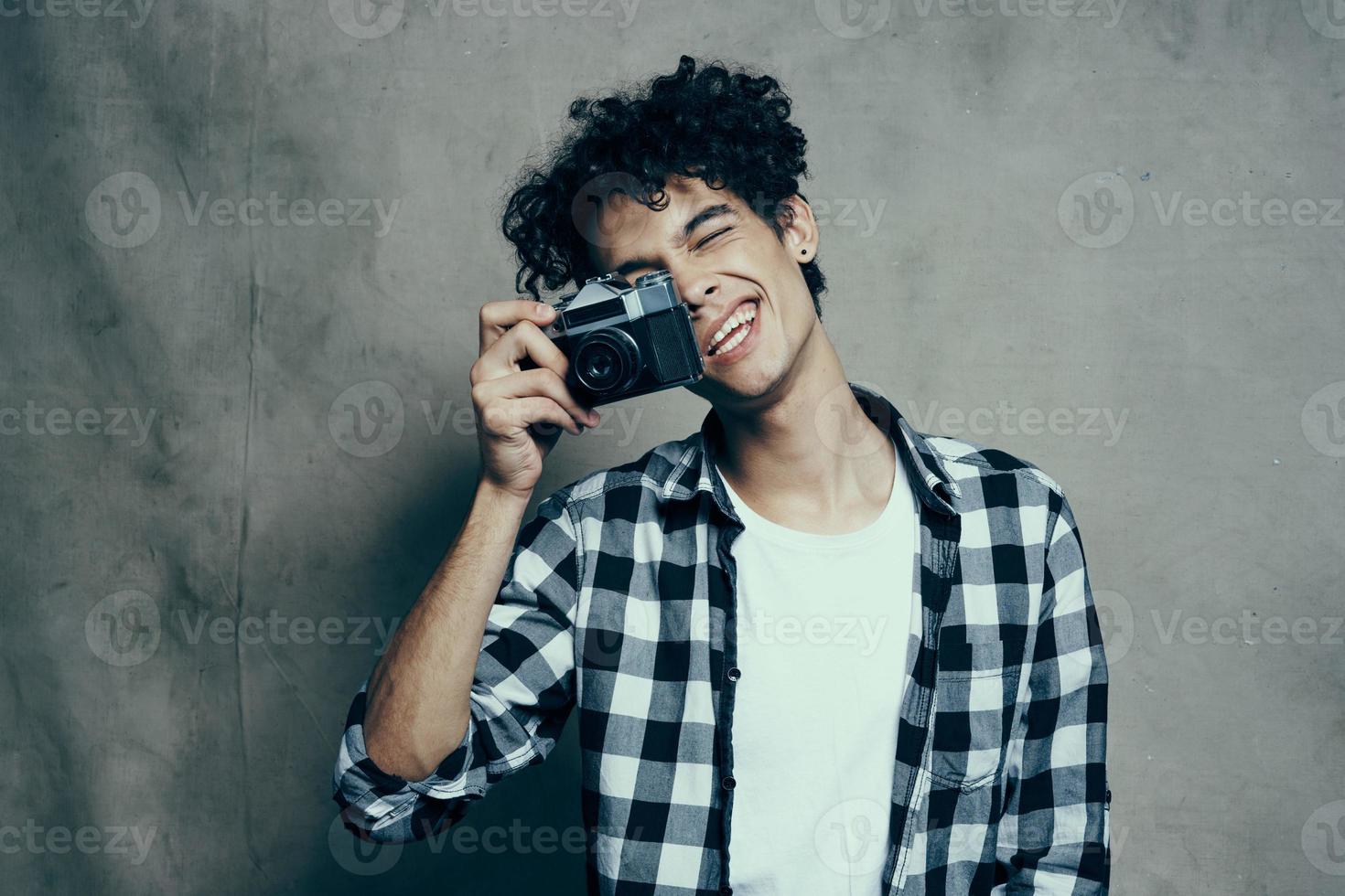 fotograf i en pläd skjorta med en kamera i hans hand på en grå bakgrund i en hobby studio rum foto